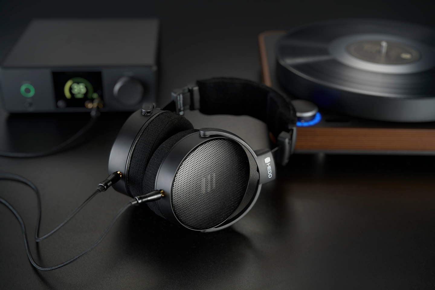 Pair of HEDDphone D1 on a dark surface with audio equipment in the background